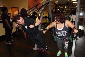 A trainer and high school student do air pushups on the TRX machine in the weight room at the JCC.